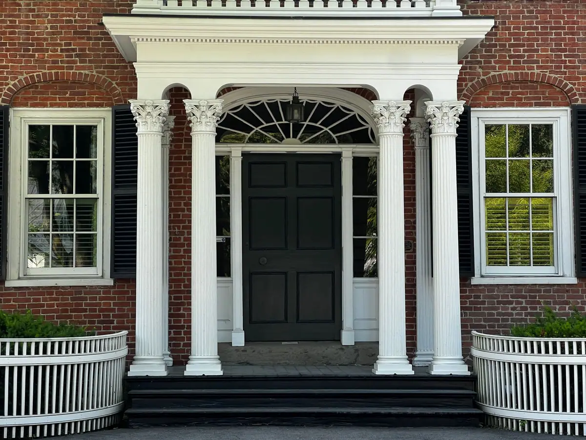 Colonial front entrance with white columns, a black door and black shutters
